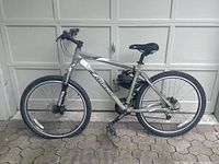 Full right-side view of silver Giant Iguana mountain bike leaning against garage door