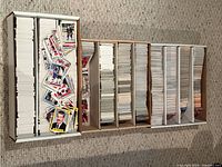 Wide overhead shot of multiple long cardboard boxes filled with stacks of hockey cards in white card sleeves, with some scattered cards on top showing player images and statistics.