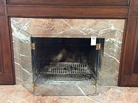 Front view of the MCM glass fireplace screen with brass hardware in place in a fireplace opening, showing the clear glass and brass hinges.