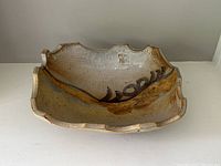 Front angle of hand thrown pottery bowl showing abstract slip glaze design and incised mark on bottom.
