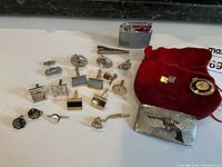 Full lot display of cufflinks, lighter, tie pin, belt buckle, pendant watch, and Cartier pouch