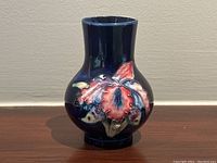 Front view of miniature Moorcroft orchid vase with pink and red orchid floral design on deep blue background.