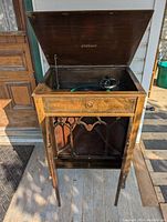 Antique record player inside a wooden cabinet with open lid, showing the turntable and needle.