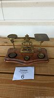 Front view of antique postal scale showing brass weighing plates, wooden base, and three brass weights placed on the base.