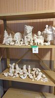 Shelves displaying a collection of white ceramic figures including animals, holiday-themed pieces, and human characters. Pieces vary in size up to approximately 11 inches.