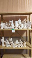 Two shelves filled with various unpainted bisque ceramic items including animals, human figurines, and decorative shapes ready for painting.