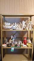 Full view of metal shelf with two shelves of assorted ceramic pieces including bowls, animal figures, and painted figurines like angels and children.