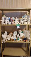 Full view of two shelves filled with assorted ceramic pieces including painted and unpainted figurines and pottery pieces.