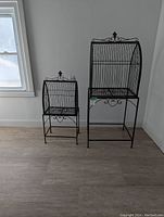 Both decorative black metal bird cages side by side, showing size difference and stand bases.