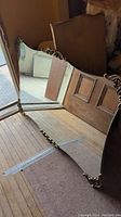 Full view of the large rectangular vintage mirror laid flat on the floor showing scalloped edges and decorative metal trim at the bottom.