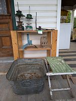 Wide view of the lot showing wooden plant stand, metal wash basin, green folding stool, and two green Coleman lanterns with metal hangers.