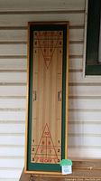 Full view of the Carrom shuffleboard tabletop board against a siding wall showing the playing surface with red markings.