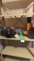 Shelf view showing enamelware ice bucket, black enamelware pot, coffee cups, cutlery block, cast iron pan