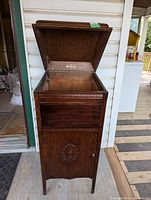 Front view of the antique Vitrola wooden cabinet with lid open showing inside storage compartment and wood grain.