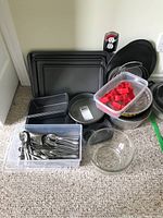 Full view of assorted bakeware including cookie sheets, pans, pizza pan, glass bowl, red cookie cutters container, and bin of kitchen cutlery.