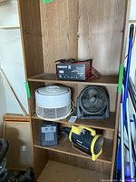 Shelf displaying PowerFist battery charger, white Honeywell air cleaner, small black fan, and two heaters (black and yellow heater, and small black heater)