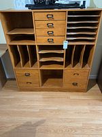 Front view of the wooden cabinet showing four small central drawers, two larger bottom drawers, and several vertical and horizontal slots for storage.
