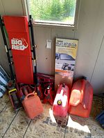 Wide view showing tall Torin Big Red hydraulic jack, plastic gas cans, sun shade box, and red bottle jacks.