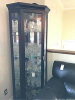 Front view of tall corner cabinet with glass door and visible glass items inside.