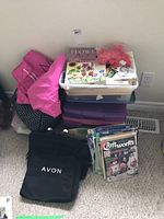 Stack of four bins with scrapbooking and craft materials, five empty purple bins, and Avon bags placed on the floor.