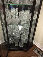 Overall view of the lot in a glass display cabinet showing multiple crystal and glassware items including pitchers, bowls, and vases.