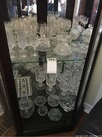 Shelf view showing multiple stemmed glasses, crystal cookie jar with lid, and other serving pieces with intricate cut patterns.