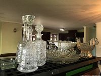 Crystal decanter, two glass decanters, glass serving platters, pedestal cake plate, and two centerpiece bowls displayed on table