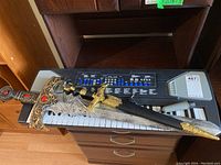 Keyboard with attached microphone and two decorative swords placed on top, showing the full keyboard and one sword's detailed hilt and sheath.