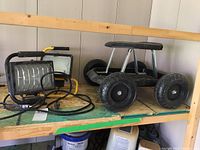 Two work lights with cords, and rolling seat on wooden shelf showing wear and age