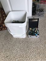 White plastic bucket filled with multicolored marbles and small silver metal case with marbles beside it