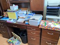 Photo showing white printer, stacks of paper, notebooks, plastic bins, tape dispenser, and office desk with drawers.