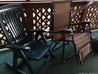Green resin rocking chair and brown antigravity chair side by side on a carpeted porch with railing in background.