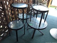 View of grouped patio tables showing four smaller tables stacked on top of larger one, all with circular glass tops and metal legs.