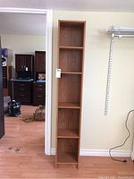 Front view of slim wooden shelf with five compartments against a wall.