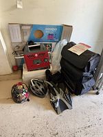 Lot photo showing Coleman HWOD water heater in original box, two bicycle helmets (one painted with a colorful splatter pattern, another silver and black), men's diving fins, snorkel, and black motorcycle sissy bar bag.