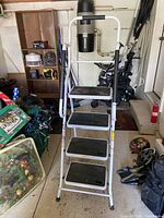 White steel platform stepladder with four steps, black slip-resistant treads, and handrails, shown folded and unfolded in a garage setting.