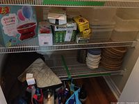 View of entire shelf showing Jelly Belly cotton candy machine box, FoodSaver kits, plastic containers, and wicker plate holders with age wear.