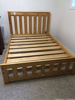Full view of natural wood full-size bed frame showing slatted headboard, footboard, and mattress support slats.