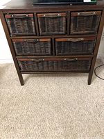 Full front view of dark brown wood cabinet with seven wicker drawers and leather-like handles.
