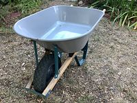Showcasing overall wheelbarrow with gray metal tray, black pneumatic tire, green frame, and wooden components.