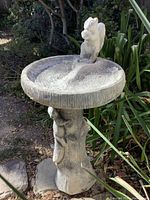 Full view of birdbath showing round basin and squirrel figure on rim with pedestal base in garden setting