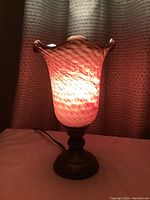 Lit dark wine colored glass table lamp with ruffled edges and gold tone metal base.