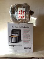Photo of the extra basket wrapped in bubble wrap labeled 'Extra Airfrier Basket' resting on top of the original Gourmia air fryer box.