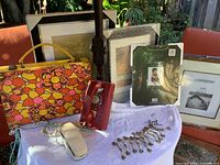 Front view of the lot showing colorful 60s briefcase, five picture frames in background, red rotary dial phone, white push-button phone, and metal cupboard hardware placed on white cloth.