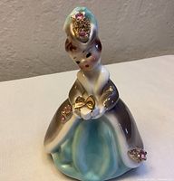 Front view of the Josef Originals porcelain tilt head doll figurine showing detailed dress and face features with jeweled accents and gift in hands.