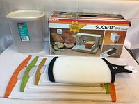 Photo showing Krups Slice/It electric food slicer in box, Rubbermaid container, and four cutting boards stacked with colored edges visible