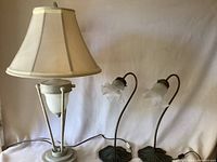 Full view of the large lamp with cream fabric shade beside two smaller lamps with curved stems and lily pad metal bases.