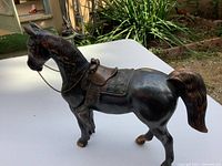 Full side view of vintage bronze/copper horse sculpture on white surface with garden background.