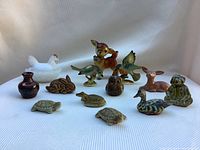 Photo showing a group of assorted vintage miniature animal figurines including deer, birds, turtles, and others on a white cloth background.