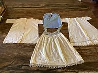 Photo showing the full set including three nightgowns, one crocheted dress with lace trim, and a blue bib
